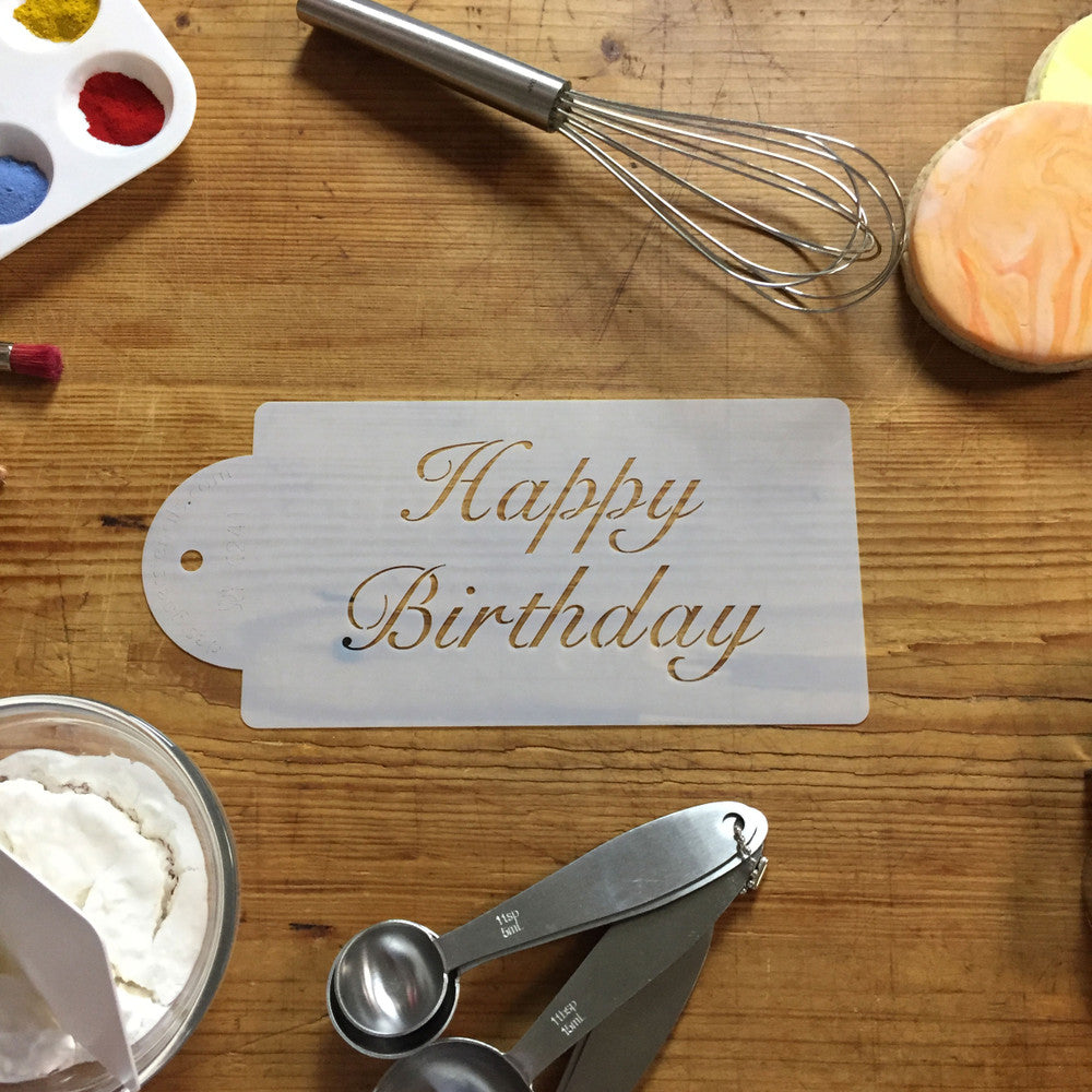 Fancy Happy Birthday cake stencil on a wooden table with baking tools and colored icing.