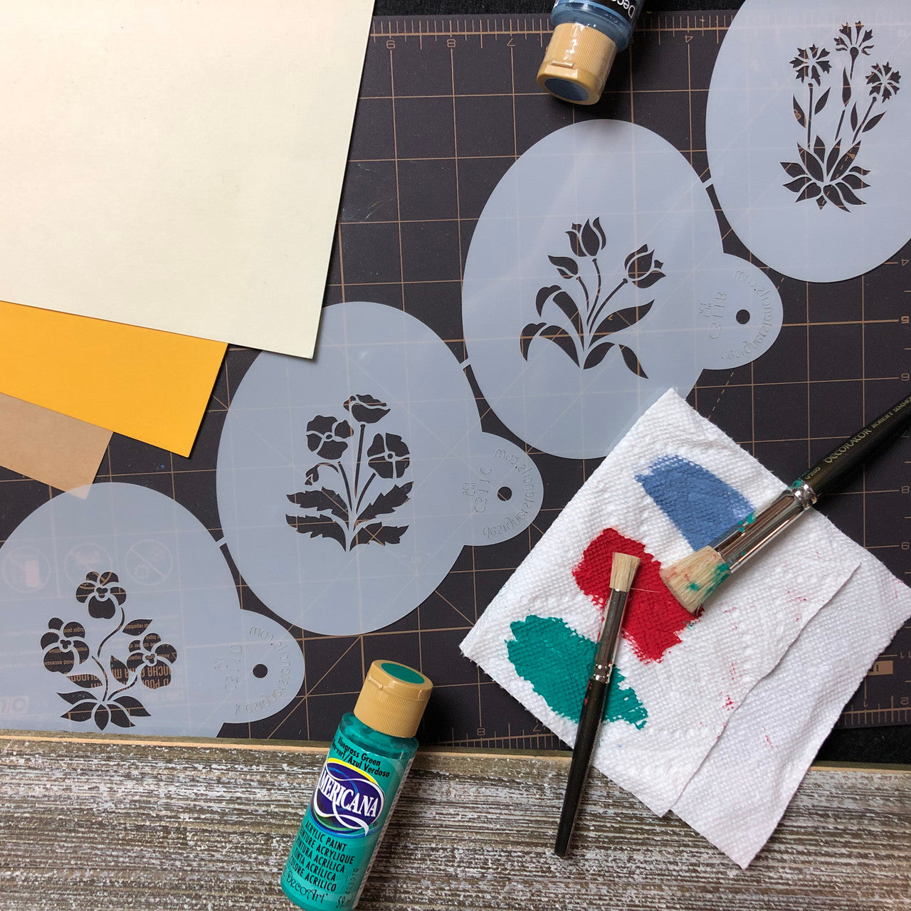 Spring Garden Cookie Stencil Set featuring floral designs, paint, and brushes on crafting table.