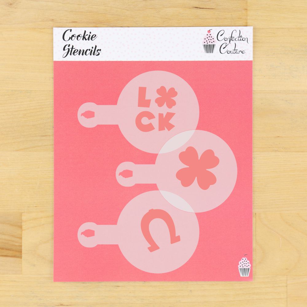 St. Patrick's Day cookie stencils set featuring designs of 'Luck', a clover, and a horseshoe on a pink background.