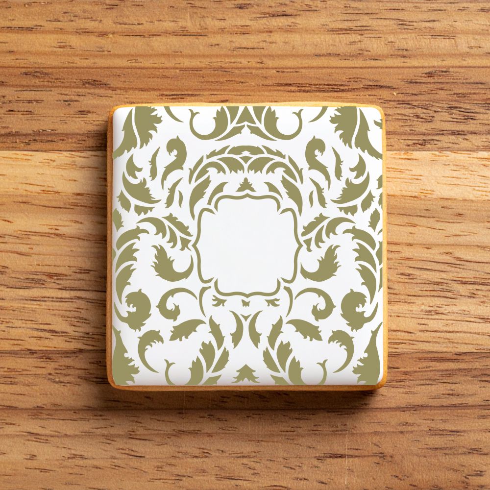 Decorative square cookie stenciled with green pattern on a wooden surface