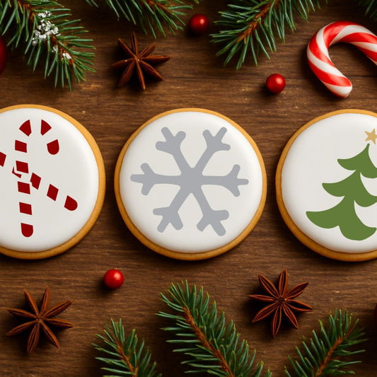 Three Christmas-themed cookies with candy cane, snowflake, and tree designs stenciled on it. Lying on a wooden surface with festive decorations.