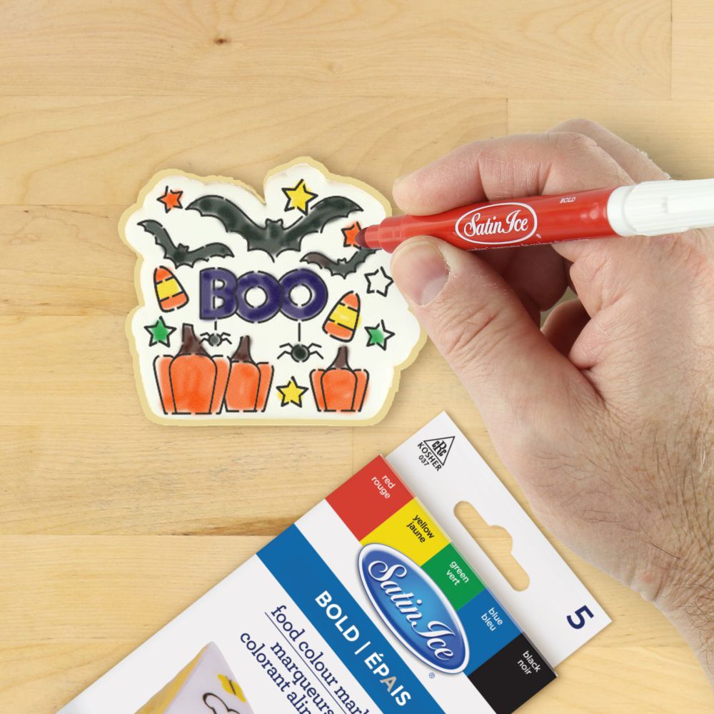 Person using a red edible marker on a decorated Halloween cookie with bats and pumpkins, showcasing the Boo stencil.