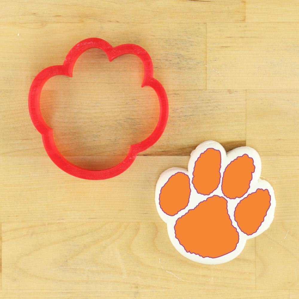 Tiger paw cookie cutter and stencil on a wooden surface, perfect for baking themed cookies for sporting events.