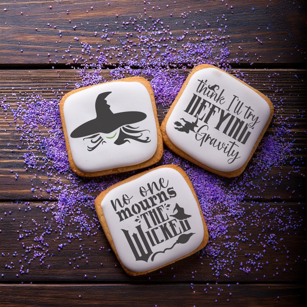 Three decorated cookies featuring Wicked-themed stencils: a witch hat, 'No One Mourns the Wicked,' and 'Defying Gravity'.