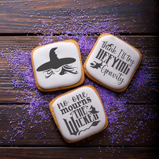 Three decorated cookies featuring Wicked-themed stencils: a witch hat, 'No One Mourns the Wicked,' and 'Defying Gravity'.
