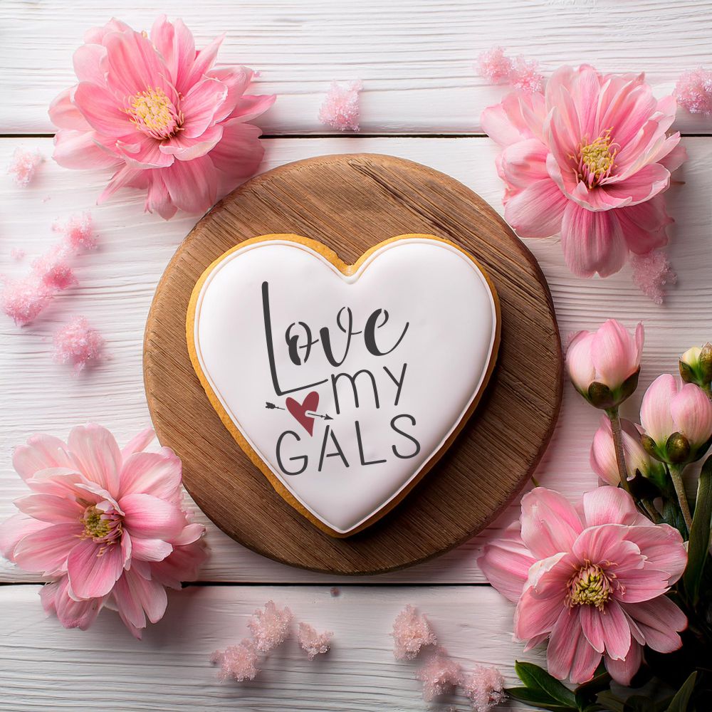 Heart-shaped cookie with 'Love my Gals' message, surrounded by pink flowers on a wooden platter.