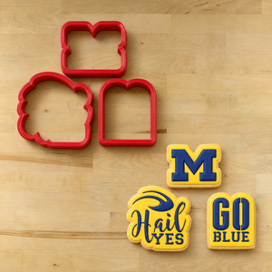 Michigan Wolverines Cookie Cutters lying next to three cookies decorated with the matching "Hail Yes" Cookie Stencil Set