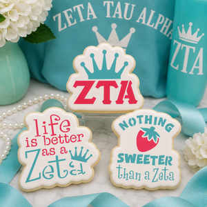 Three decorated ZTA-inspired sugar cookies with crown and strawberry designs displayed with turquoise sorority-themed décor.