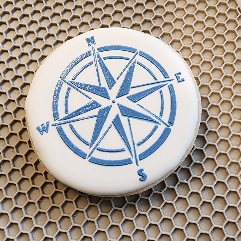 White cookie with blue compass design on a textured surface