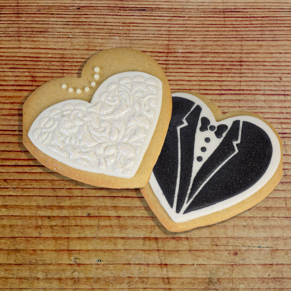 Bride and groom heart-shaped cookies decorated with floral and tuxedo designs, ideal for wedding celebrations.