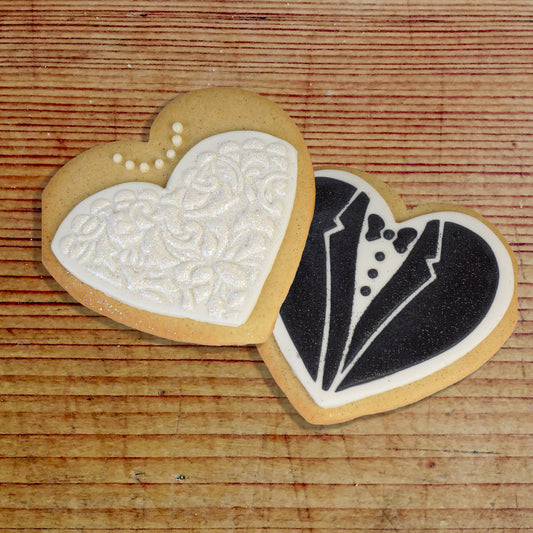 Bride and groom heart-shaped cookies decorated with floral and tuxedo designs, ideal for wedding celebrations.