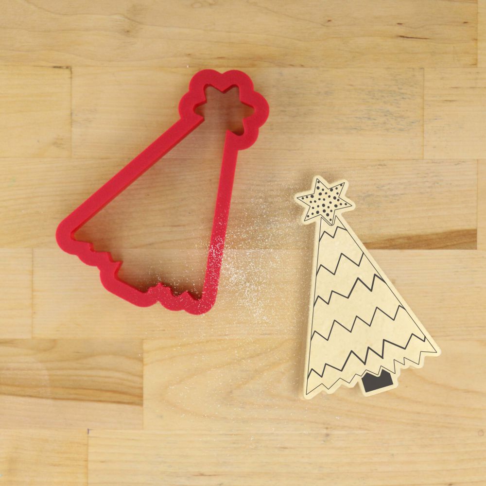 Red Christmas tree cookie cutter and wooden stencil on a wooden surface for holiday baking.