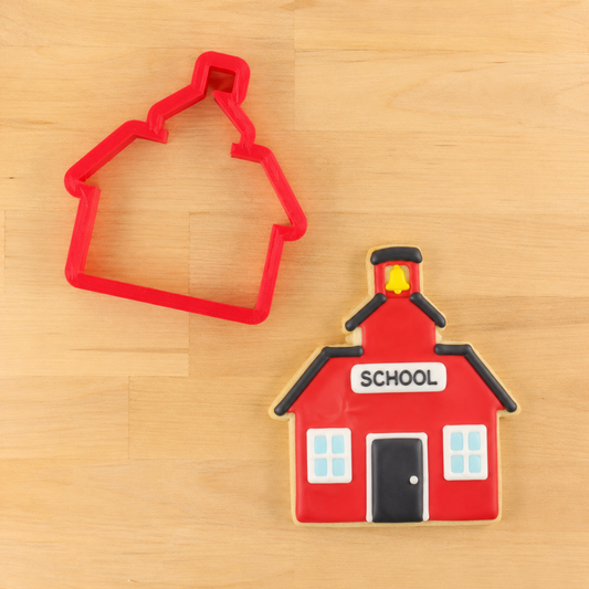Red schoolhouse cookie cutter with decorated schoolhouse cookie