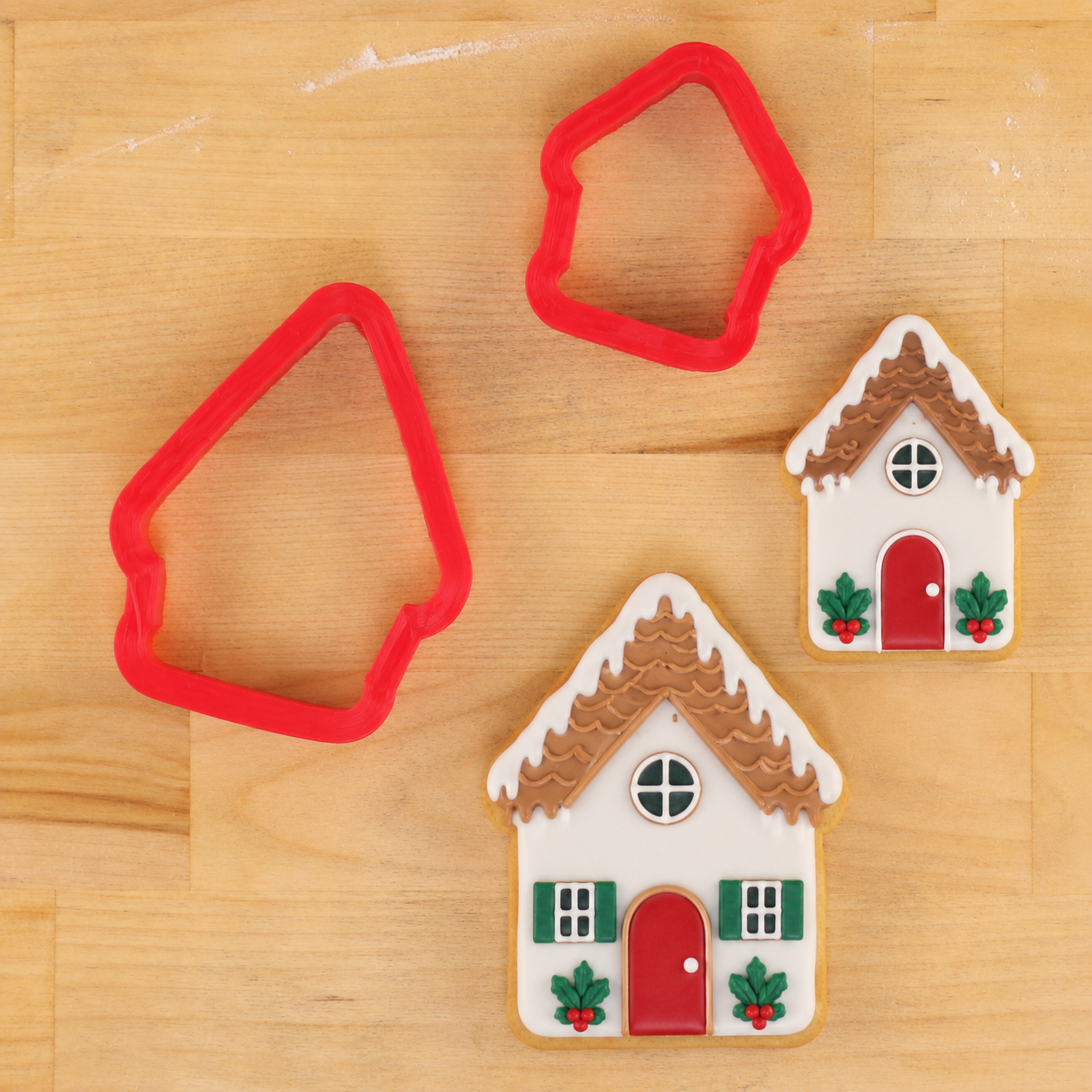 House-shaped cookie cutters next to house-shaped cookies iced and decorated for the holidays
