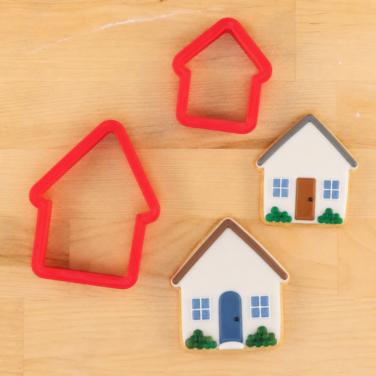 House-shaped cookie cutters next to house-shaped cookies decorated for a housewarming party. 