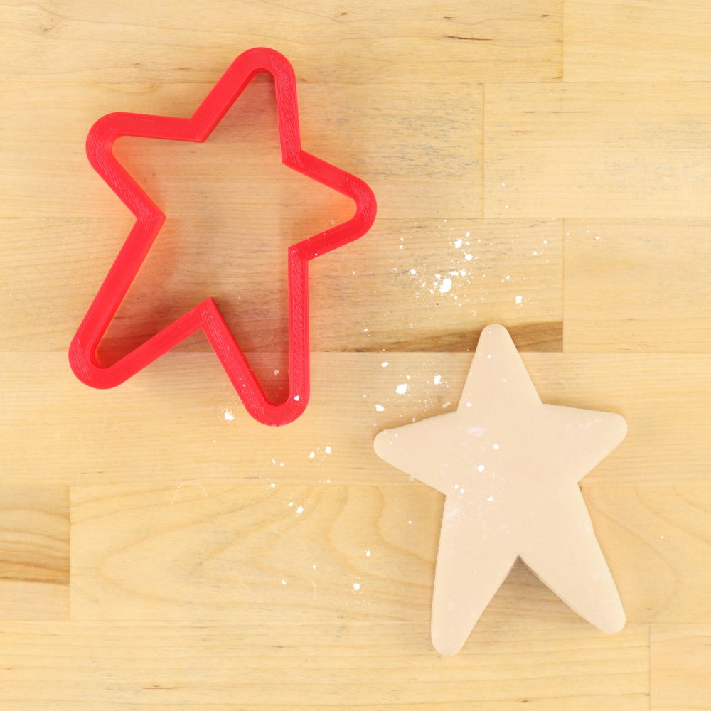 Red star cookie cutter beside a freshly cut star-shaped cookie on a wooden surface.
