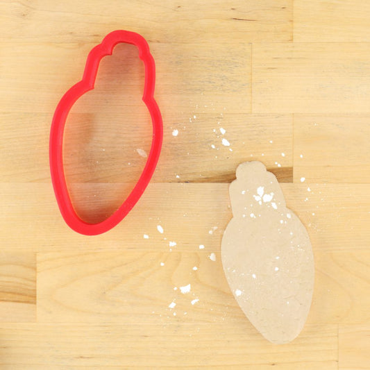 Cookie cutter shaped like a light bulb with colored sections on a wooden surface.