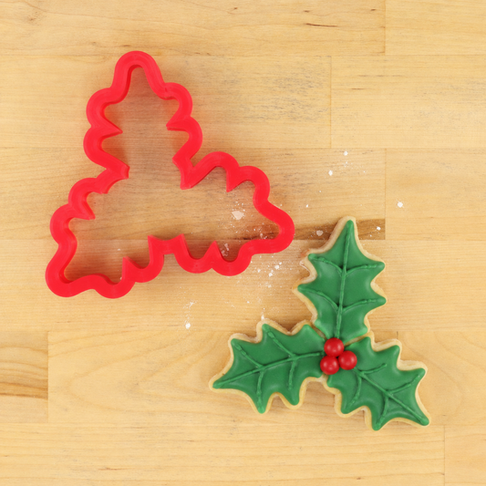 Holly Leaf Christmas Cookie Cutter next to a holly leaf Christmas cookie decorated with green icing and red berries