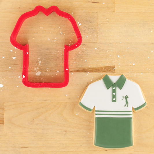 Cookie cutter shaped like a collared shirt next to a cookie shaped like a collared golf shirt on a wooden surface
