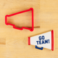 Red megaphone-shaped cookie cutter on a wooden surface with 'GO TEAM!' megaphone shaped cookie.