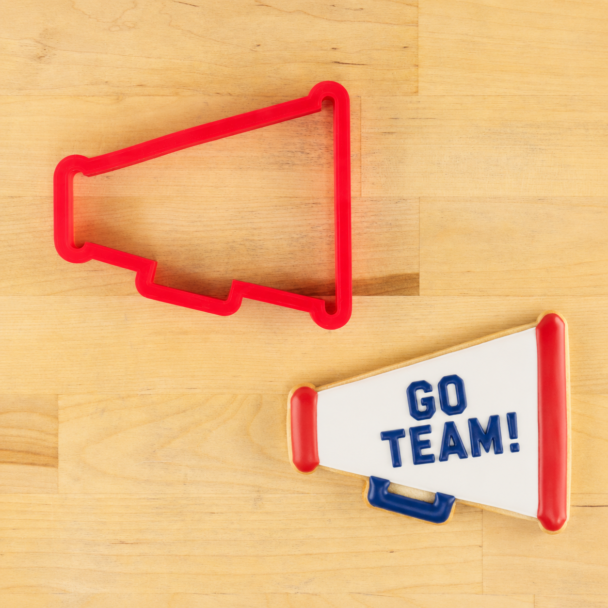 Red megaphone-shaped cookie cutter on a wooden surface with 'GO TEAM!' megaphone shaped cookie.