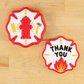 Two decorative patches on a wooden surface, one with a fire hydrant and ladder design, the other with 'THANK YOU' text.