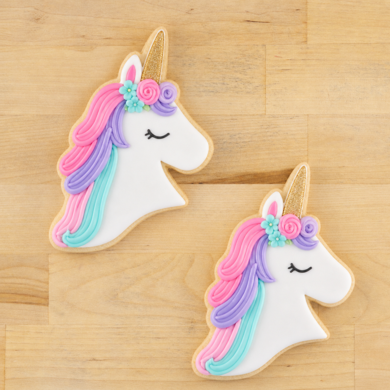 Two unicorn-shaped cookies with colorful icing on a wooden surface
