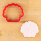 Shell-shaped cookie cutter with a decorated shell cookie lying next to it.