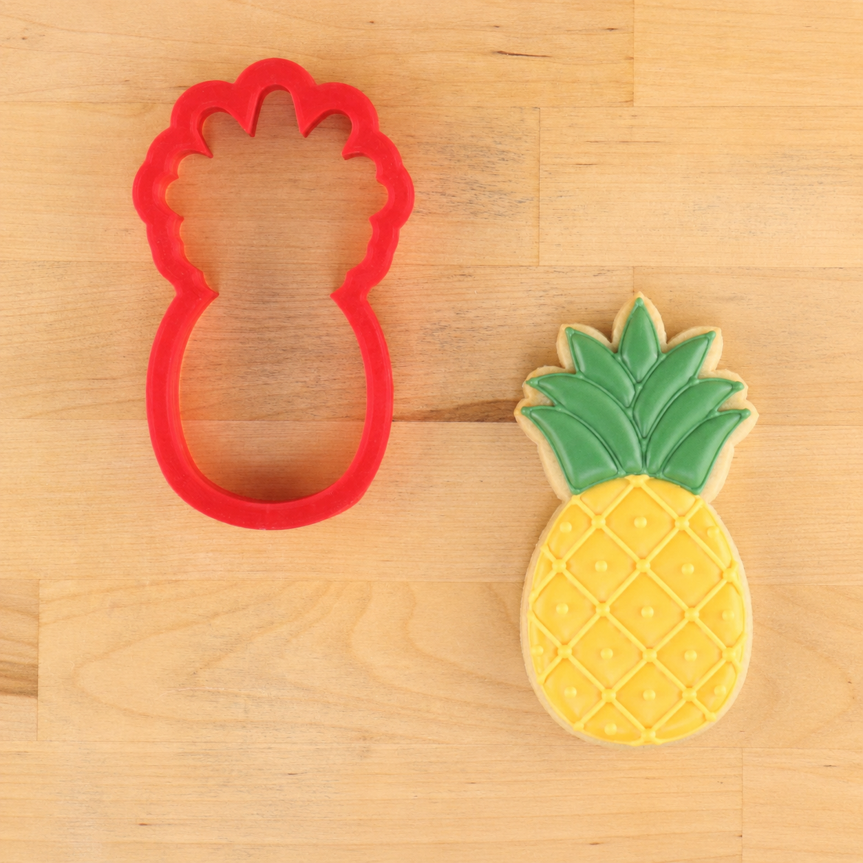 Pineapple-shaped cookie cutter with a pineapple-shaped cookie on a wooden surface