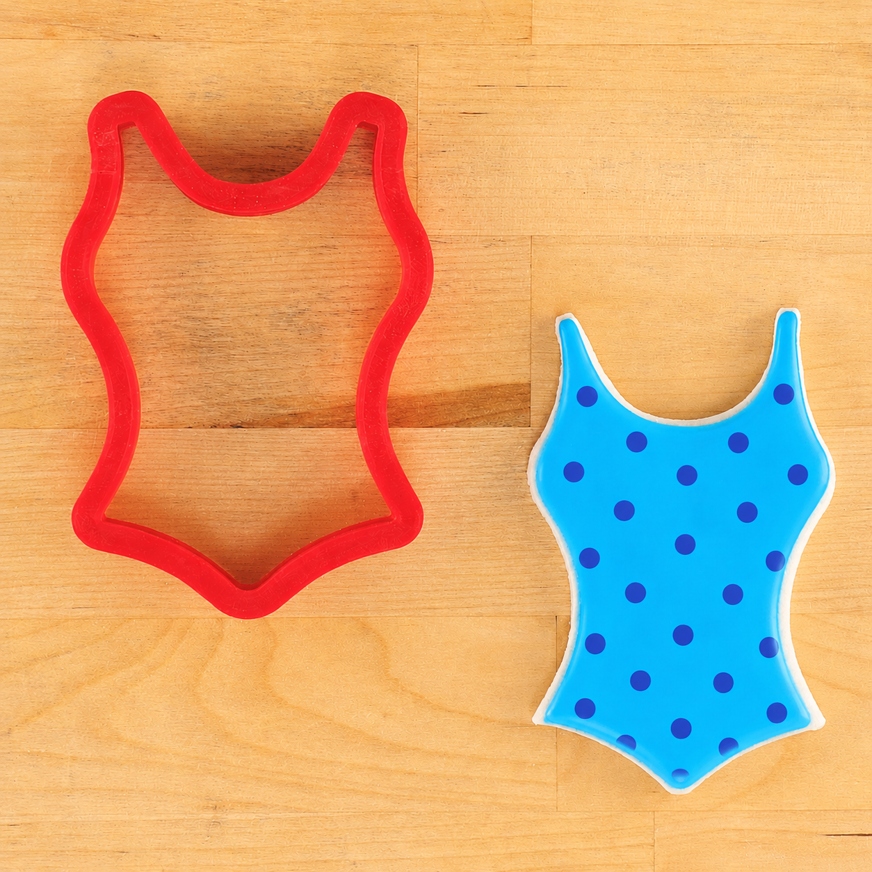 Red cookie cutter shaped like a swimsuit and blue swimsuit with polka dots on a wooden surface