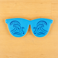 Sunglasses shaped cookie with ocean wave cookie stenciled applied to the the top