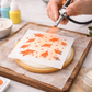 Person using an airbrush to apply the graduation cap cookie stencil onto a white iced cookie.