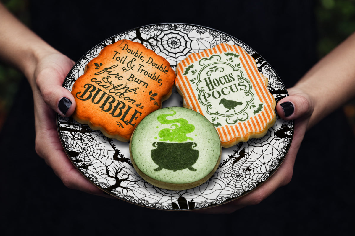 Halloween-themed cookies on a decorative plate held by hands with black nail polish.