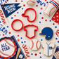 Baseball cookie cutters and baseball shaped cookies with a baseball party backdrop.