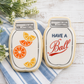 Two cookies shaped like mason jars with decorative elements on a wooden surface.