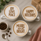 Three cups of coffee with festive text on the foam, surrounded by coffee beans and a gift box.