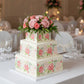 Three-tiered floral cake with pink roses on a white background
