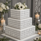 Three-tiered square wedding cake with polka dot pattern and floral top, set against a decorative background.