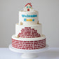Three-tiered cake with 'Welcome Home' text and house decoration on a white background