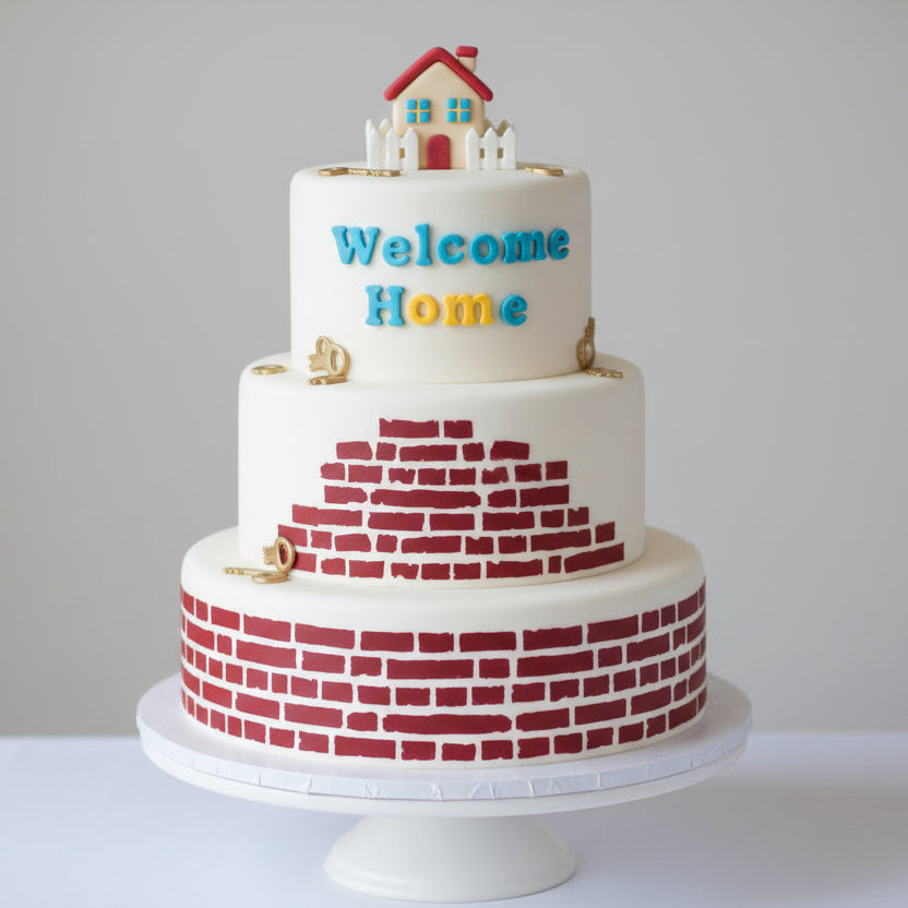 Three-tiered cake with 'Welcome Home' text and house decoration on a white background