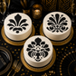 Three white cakes with black decorative patterns on a black tablecloth with gold accents.