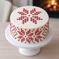 White Christmas cake with red knit-style snowflakes and diamond motifs around the sides and a matching snowflake on top.