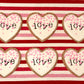 Heart-shaped cookies with 'love' writing on a red and white striped background