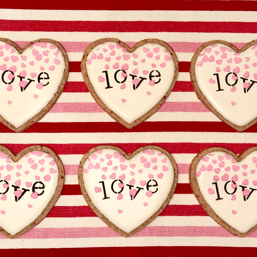 Heart-shaped cookies with 'love' writing on a red and white striped background