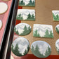 Decorative cookies with mountain and tree designs on a baking tray.
