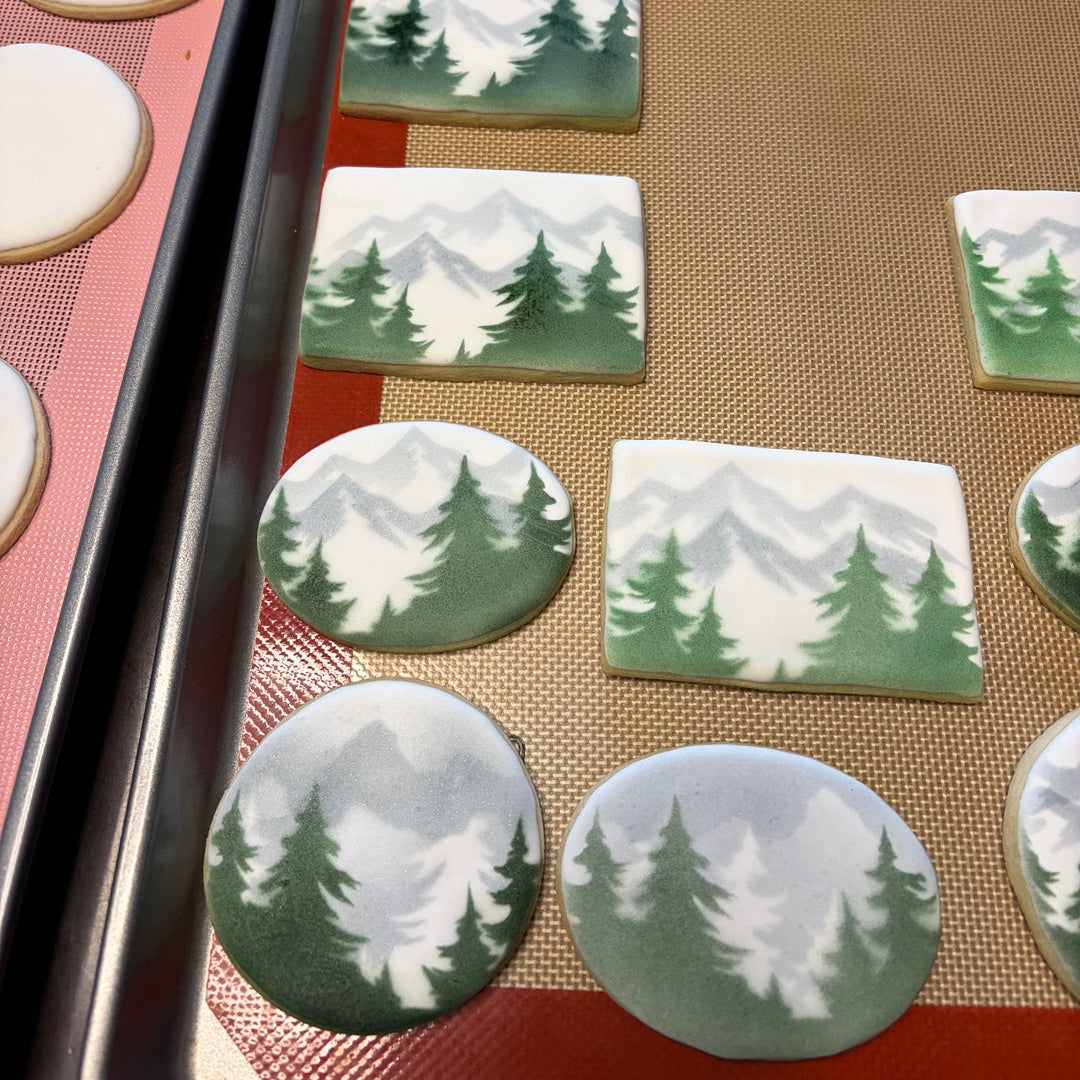 Decorative cookies with mountain and tree designs on a baking tray.