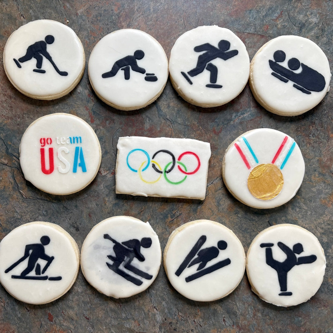 Decorative cookies with Olympic-themed designs on a stone surface
