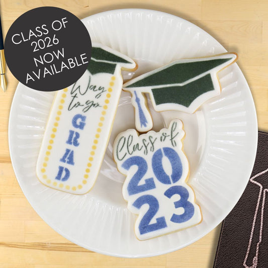 Graduation-themed cookies on a white plate with 'Class of 2026' and 'Way to go GRAD' text, set against a wooden surface.