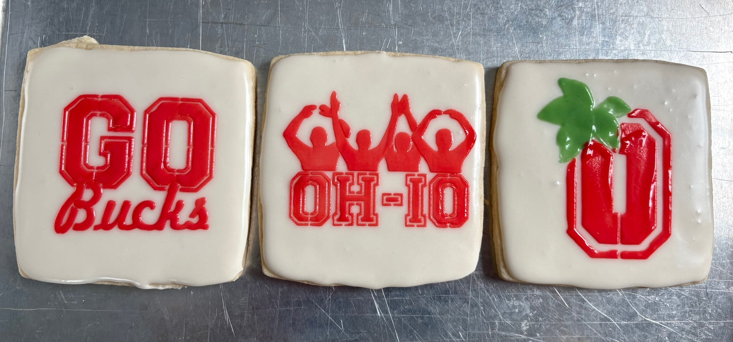 Three cookies with Ohio State-themed designs on a metal surface
