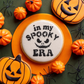 In My Spooky Era Halloween cookie stencil on a cookie surrounded by pumpkins and spiders, perfect for bakers this season.
